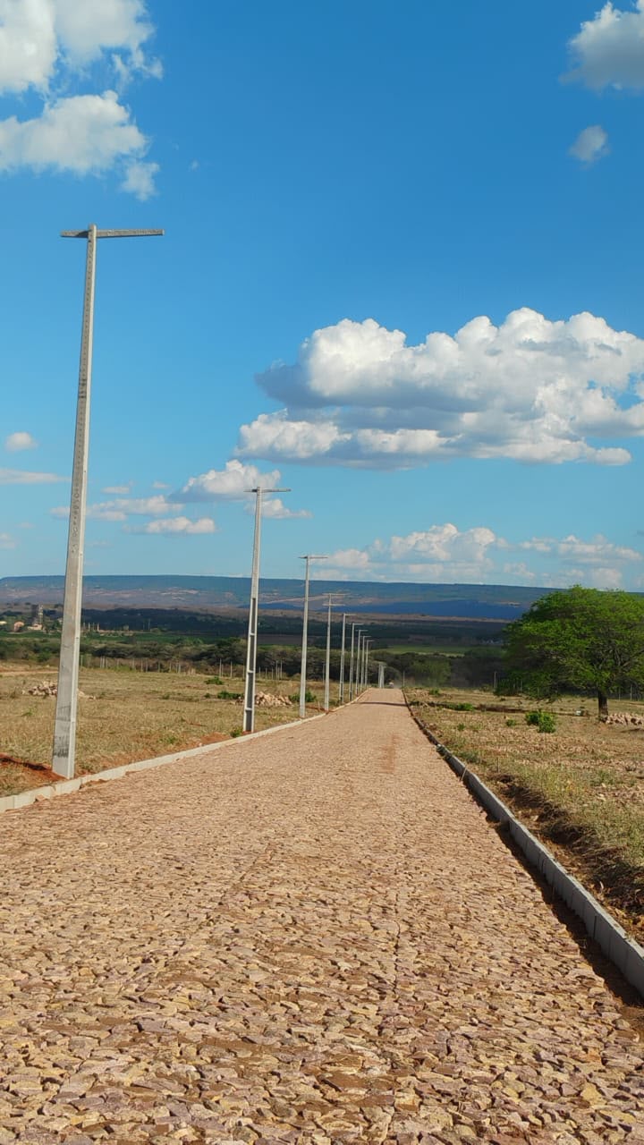 Rua pavimentada em declive com sequência de postes e paisagem ao fundo