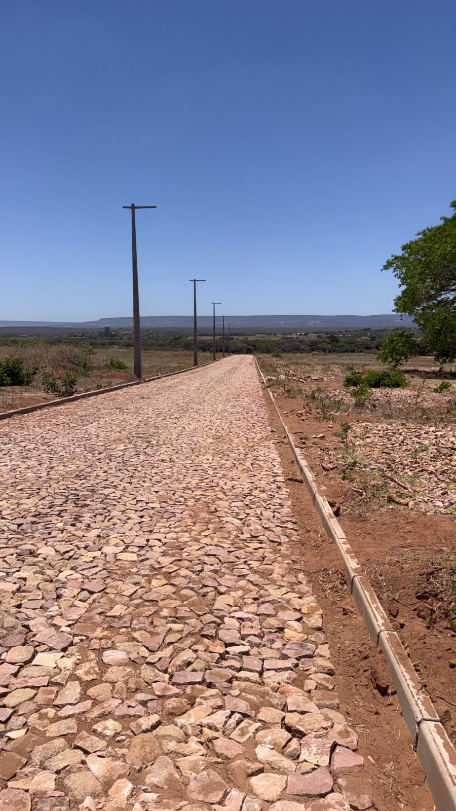 Rua de pedras com meio-fio, postes e vista do entorno do Terra Santa Canaã